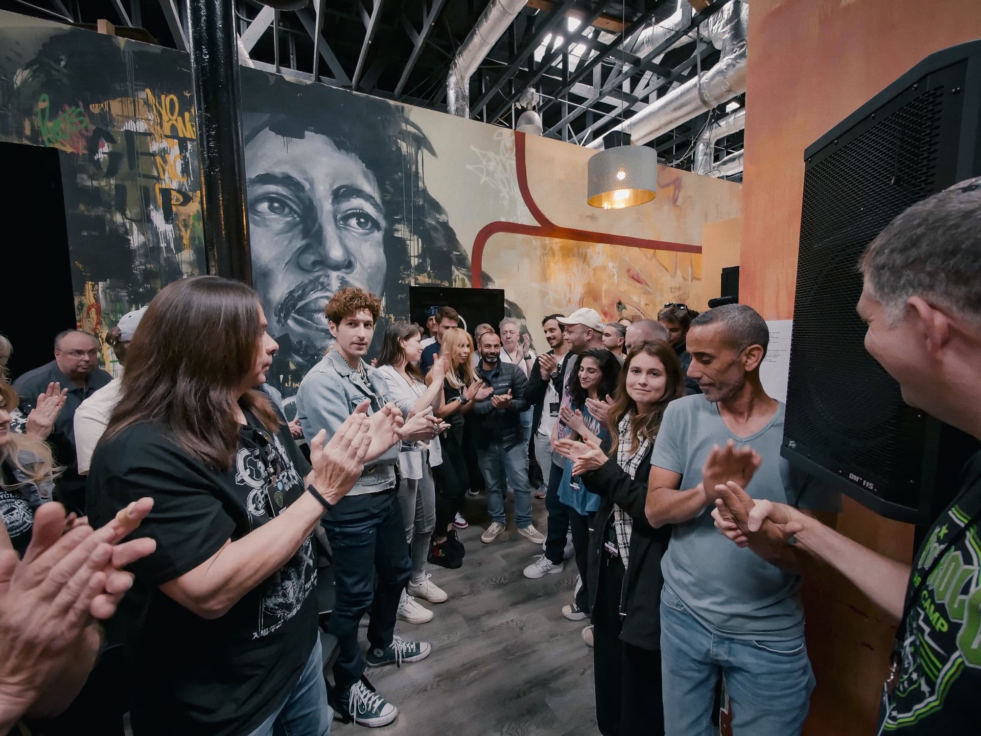 Campers and mentors applaud in a rehearsal space decorated with a Jimi Hendrix mural.