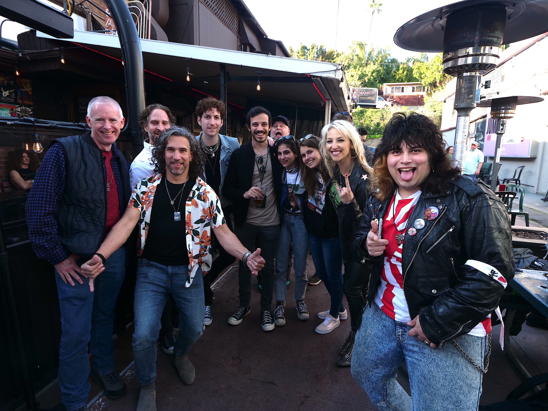 A large group of musicians and crew pose together on an outdoor patio.