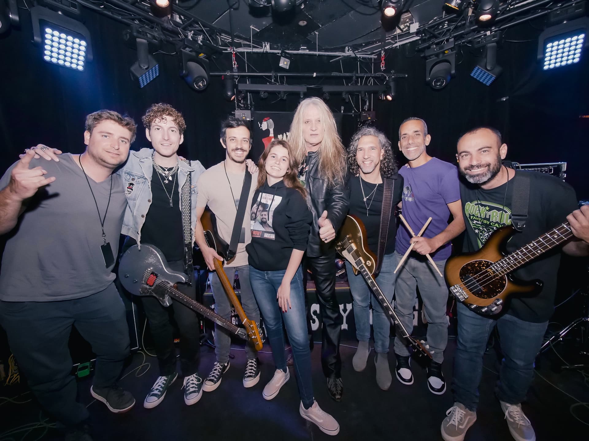 A group of musicians pose onstage at the Whisky a Go Go under stage lights.